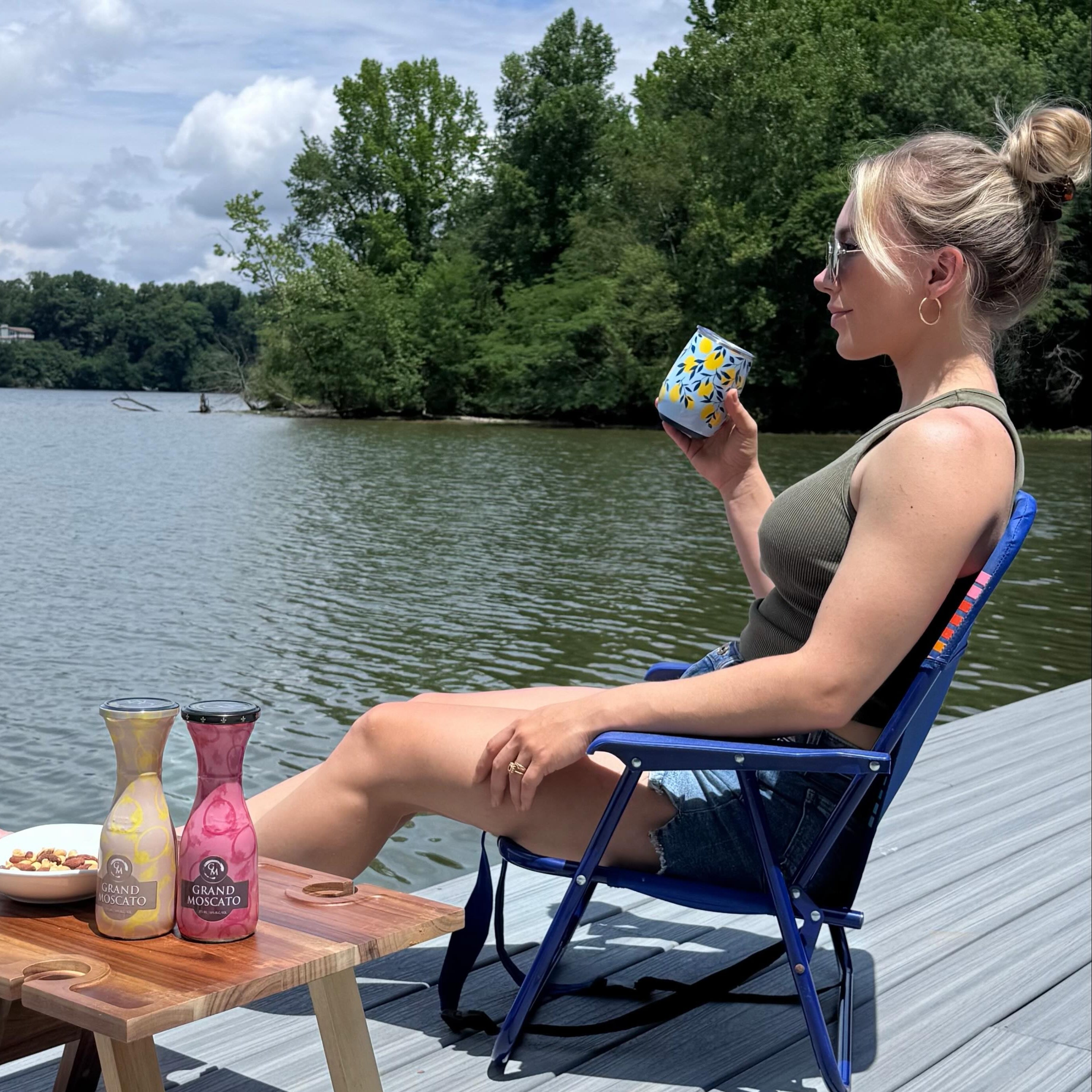 Woman sitting on a dock with glass of wine in hand and Grand Moscato minis on portable table