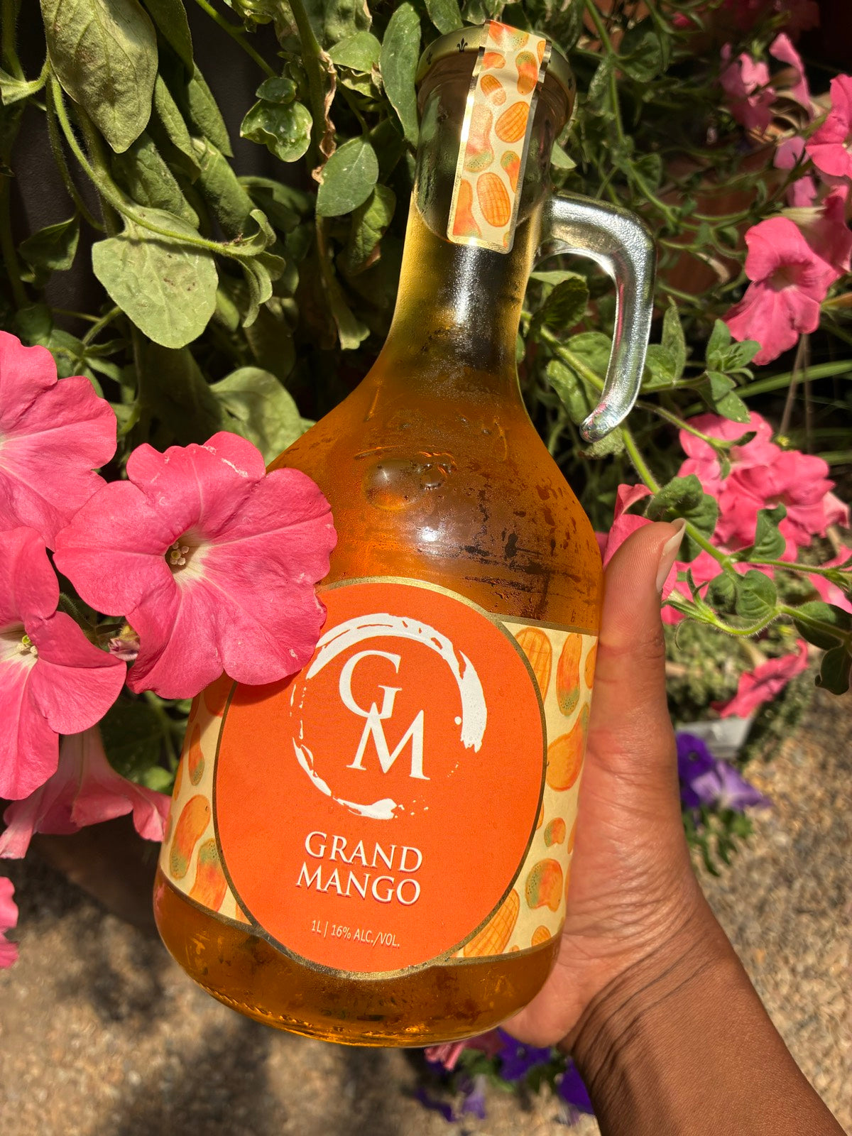 Bottle of Grand Moscato Mango held in front of pink flowers